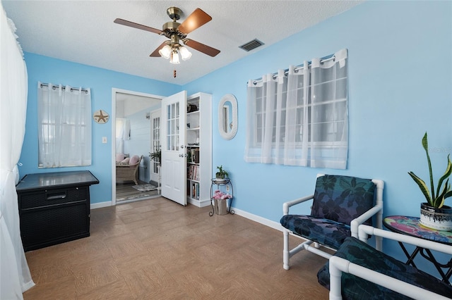 sitting room with visible vents, a textured ceiling, baseboards, and a ceiling fan