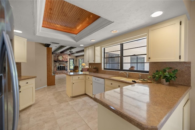 kitchen featuring tasteful backsplash, a peninsula, white dishwasher, stainless steel fridge, and a raised ceiling