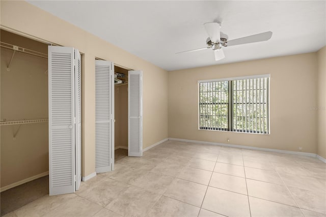 unfurnished bedroom featuring tile patterned floors, baseboards, multiple closets, and ceiling fan