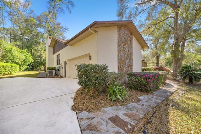 view of property exterior with stucco siding, driveway, stone siding, an attached garage, and central AC unit