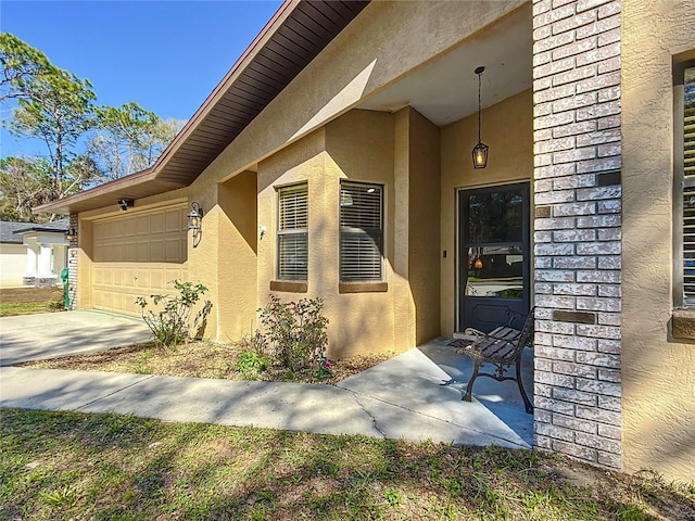 entrance to property featuring concrete driveway, an attached garage, and stucco siding