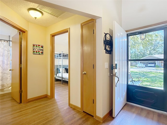 entryway with baseboards, light wood-type flooring, and a textured ceiling