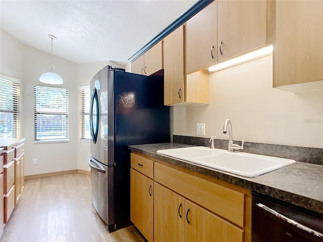 kitchen featuring dark countertops, dishwasher, light wood-type flooring, freestanding refrigerator, and a sink