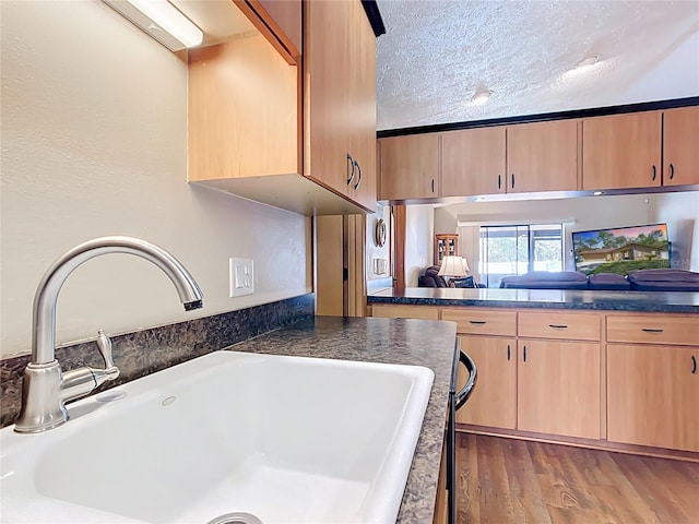 kitchen featuring a textured ceiling, wood finished floors, light brown cabinets, and a sink