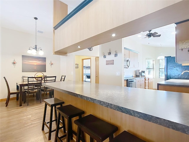 kitchen featuring a kitchen bar, ceiling fan with notable chandelier, a sink, light wood-style floors, and appliances with stainless steel finishes