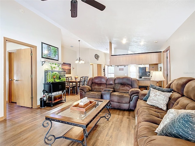 living area with light wood-style flooring, vaulted ceiling, and ceiling fan with notable chandelier