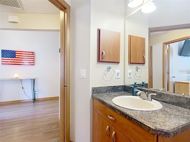 bathroom with visible vents, baseboards, vanity, wood finished floors, and a textured ceiling