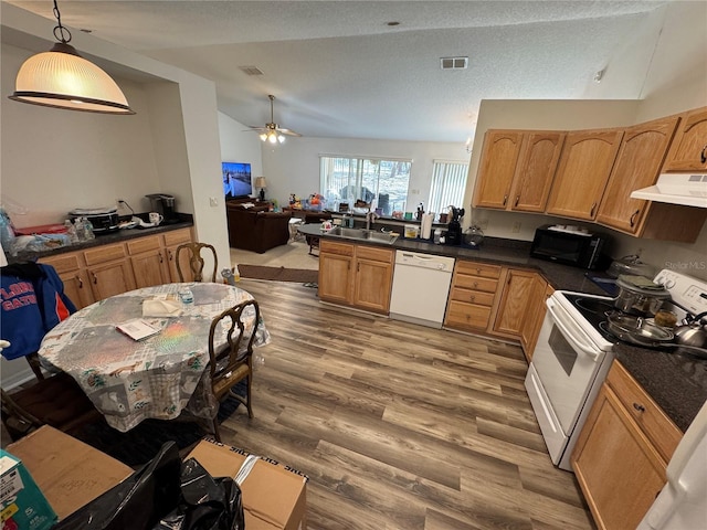 kitchen with dark countertops, visible vents, under cabinet range hood, white appliances, and a sink