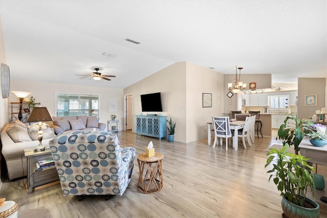 living room featuring light wood finished floors, visible vents, ceiling fan with notable chandelier, and vaulted ceiling