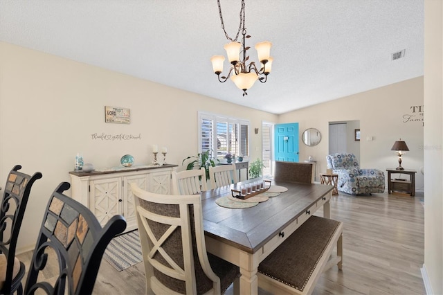 dining space with an inviting chandelier, light wood-style flooring, visible vents, and a textured ceiling