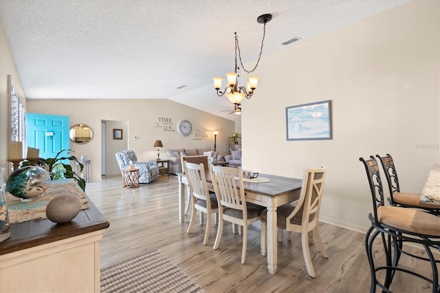 dining space with light wood-type flooring, visible vents, lofted ceiling, and a notable chandelier