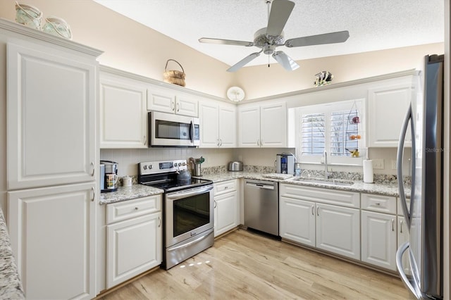 kitchen with a sink, light wood-style floors, appliances with stainless steel finishes, a textured ceiling, and white cabinetry