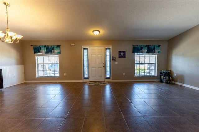 entryway with an inviting chandelier, dark tile patterned flooring, baseboards, and a textured ceiling