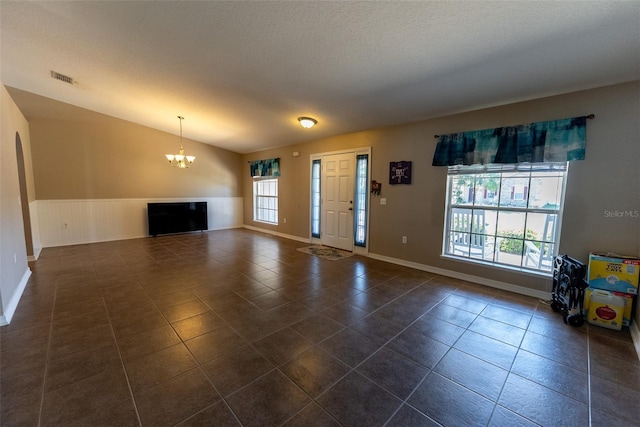 unfurnished living room with an inviting chandelier, vaulted ceiling, a healthy amount of sunlight, and visible vents