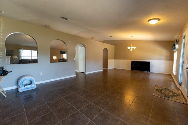 unfurnished living room with visible vents, vaulted ceiling, an inviting chandelier, a textured ceiling, and dark tile patterned flooring