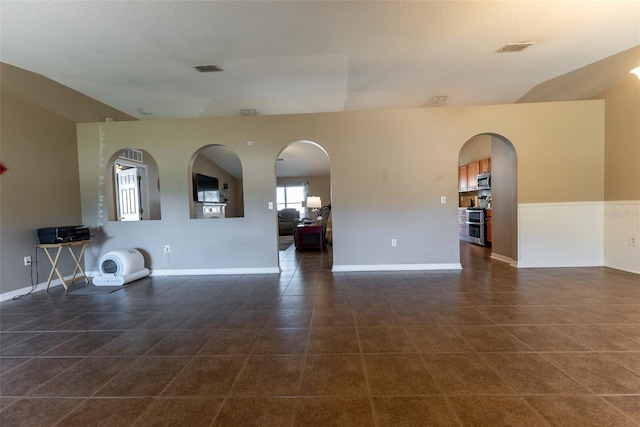 unfurnished living room with dark tile patterned floors, visible vents, and wainscoting