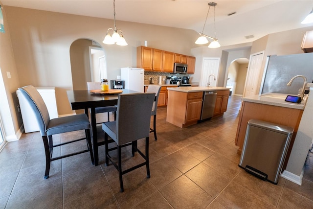 kitchen featuring a kitchen island with sink, backsplash, arched walkways, appliances with stainless steel finishes, and light countertops