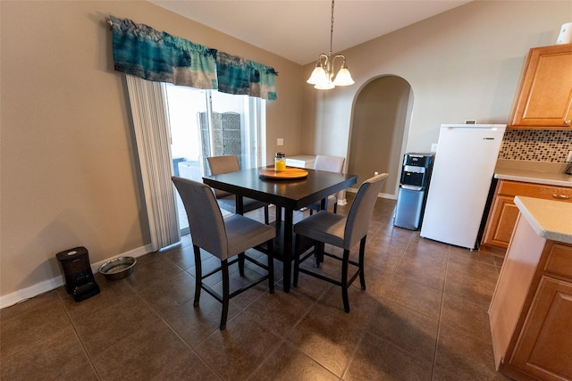 dining area featuring dark tile patterned flooring, a notable chandelier, baseboards, and arched walkways