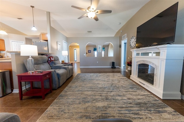 living area featuring baseboards, dark tile patterned floors, lofted ceiling, arched walkways, and a glass covered fireplace