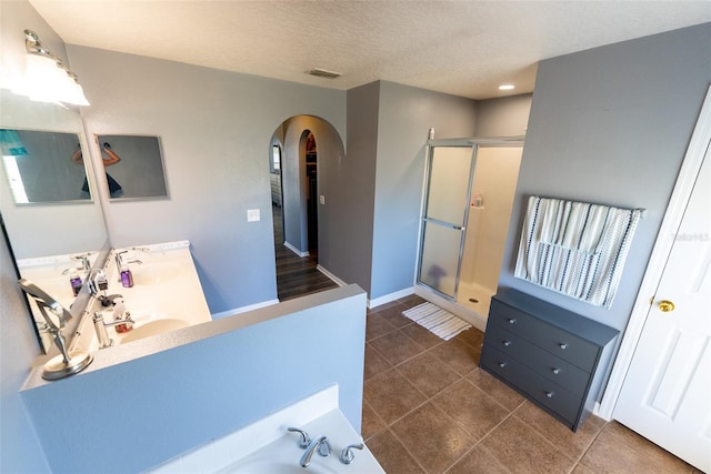 full bathroom with visible vents, a shower stall, double vanity, tile patterned floors, and a textured ceiling