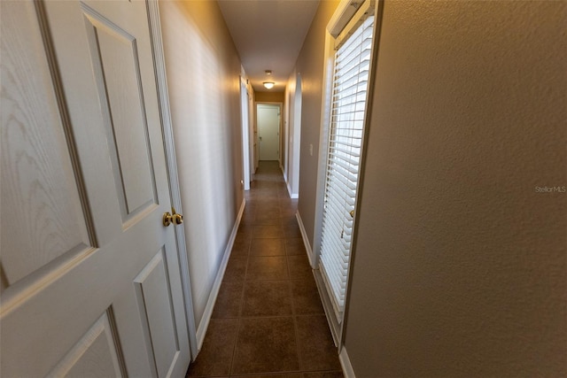 hallway with baseboards and dark tile patterned floors