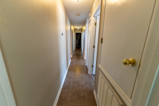 corridor with dark tile patterned floors and baseboards