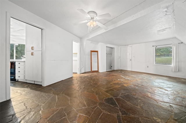 unfurnished living room featuring a textured ceiling, stone floors, a ceiling fan, and vaulted ceiling