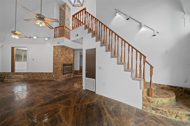 staircase with visible vents, track lighting, a glass covered fireplace, a high ceiling, and ceiling fan