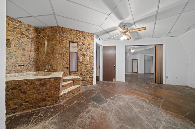 bathroom with stone flooring, a ceiling fan, a drop ceiling, and walk in shower