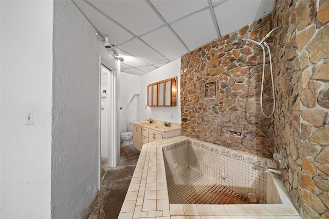 bathroom featuring toilet, a paneled ceiling, a bathtub, vanity, and a textured wall