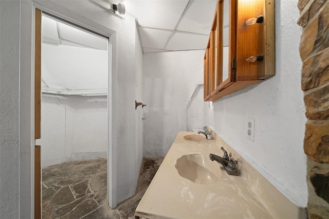 full bathroom with a walk in closet, double vanity, a paneled ceiling, and a sink