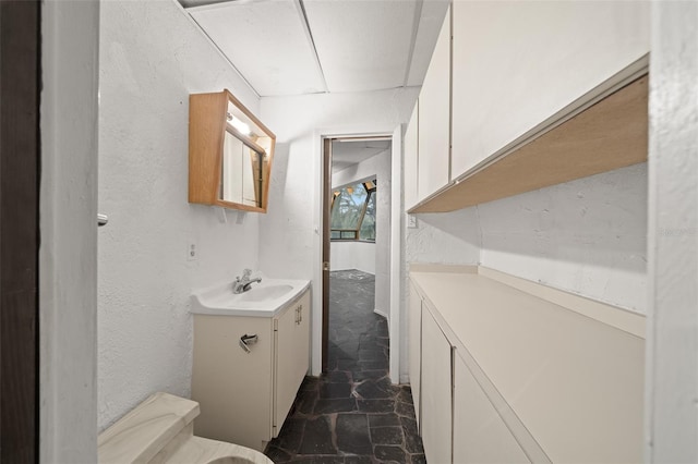 bathroom featuring vanity, toilet, a textured wall, and marble finish floor