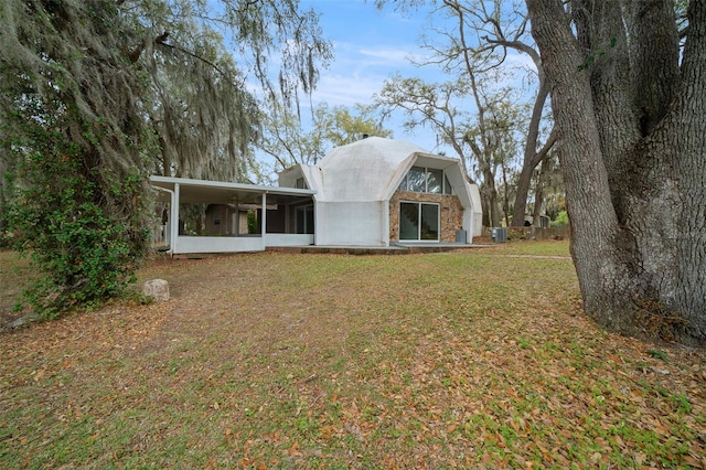 back of house with a yard, stone siding, and a sunroom