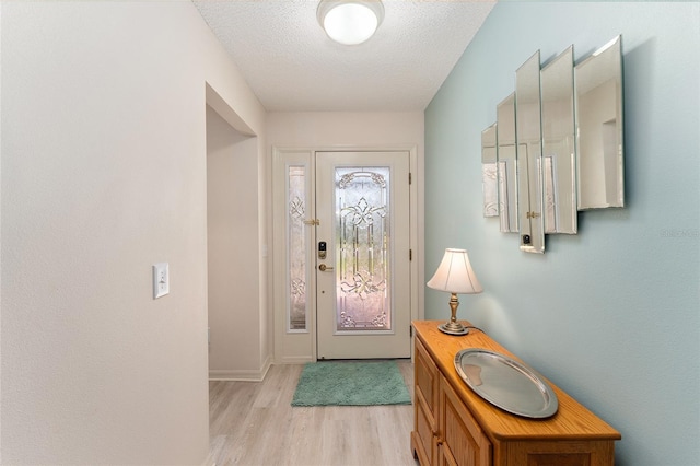 entryway featuring baseboards, light wood-style floors, and a textured ceiling