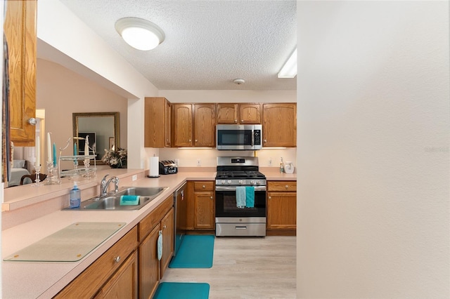 kitchen featuring light countertops, stainless steel appliances, a textured ceiling, a sink, and light wood-style floors