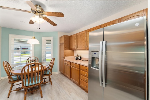 kitchen with stainless steel fridge, a textured ceiling, brown cabinetry, light wood-style flooring, and ceiling fan