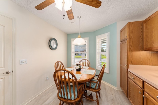 dining space with light wood finished floors, baseboards, ceiling fan, and a textured ceiling