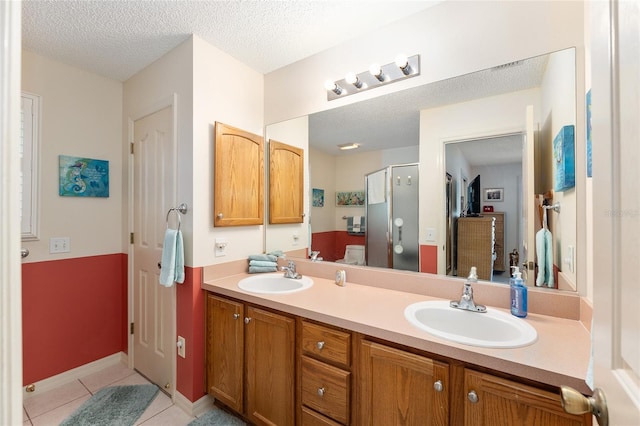 full bath with a textured ceiling, a sink, tile patterned flooring, and a shower stall