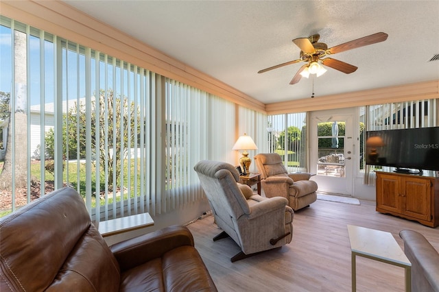 living area with light wood finished floors, a textured ceiling, visible vents, and a ceiling fan