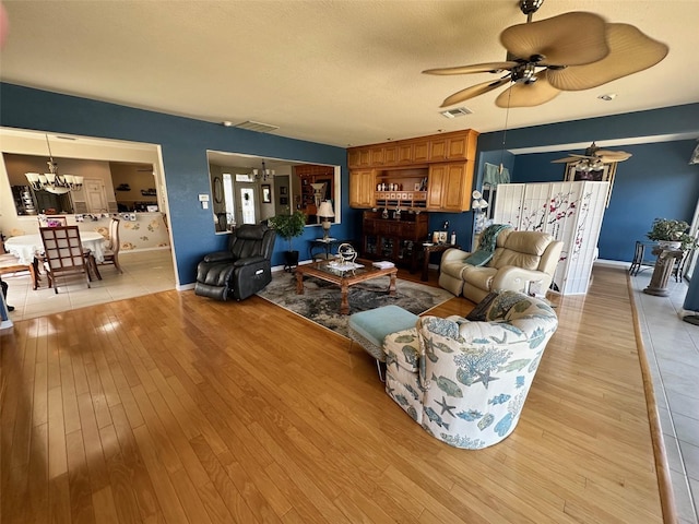 living area with ceiling fan with notable chandelier, visible vents, light wood finished floors, and a textured ceiling