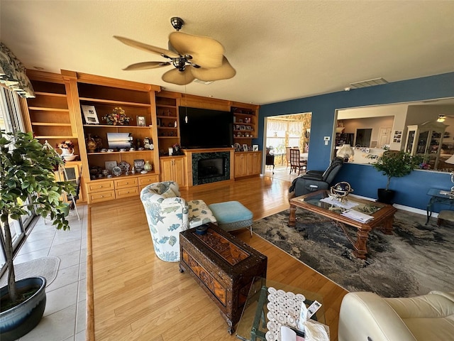 living room featuring light wood-style flooring, a ceiling fan, visible vents, and a textured ceiling
