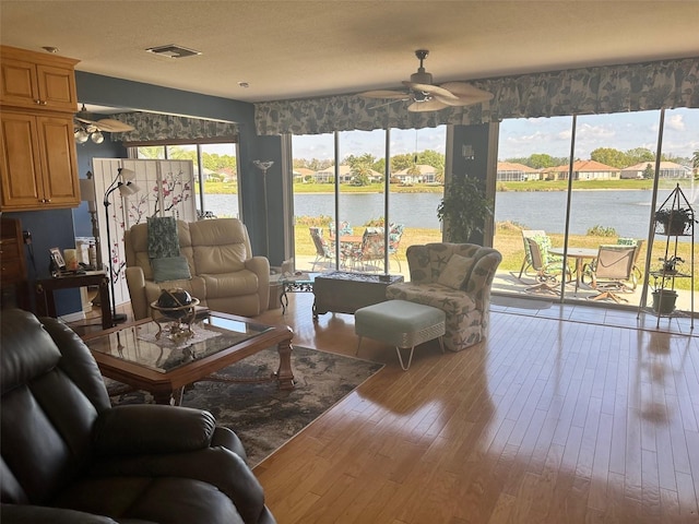 living room with wood finished floors, visible vents, a water view, and ceiling fan