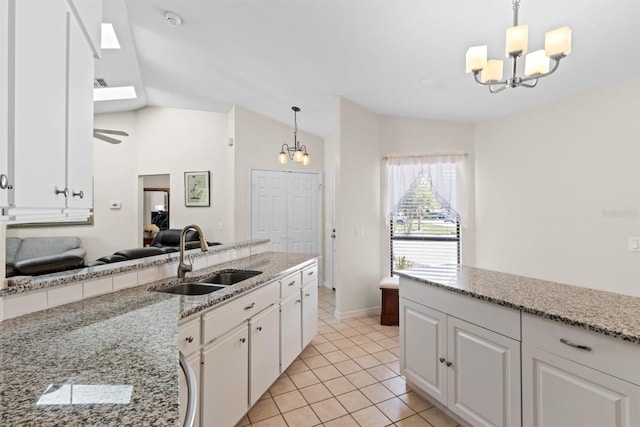 kitchen featuring vaulted ceiling with skylight, an inviting chandelier, light tile patterned flooring, white cabinetry, and a sink