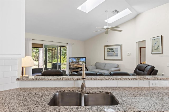 kitchen featuring visible vents, lofted ceiling, a sink, open floor plan, and light stone countertops