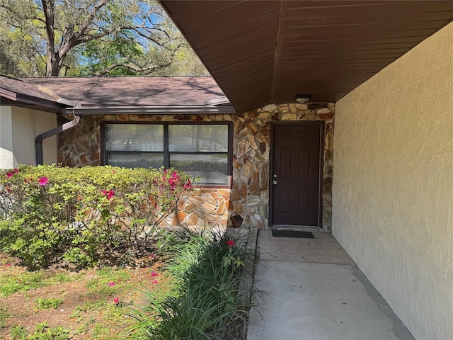 entrance to property featuring stucco siding, stone siding, and roof with shingles