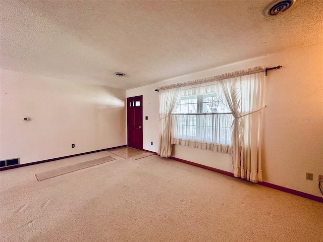 empty room with visible vents, carpet floors, a textured ceiling, and baseboards