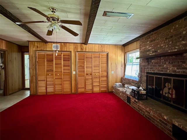 unfurnished room with beamed ceiling, visible vents, wood walls, a brick fireplace, and ceiling fan