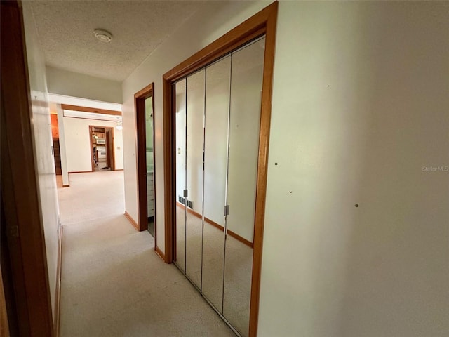 hallway with light colored carpet, baseboards, and a textured ceiling