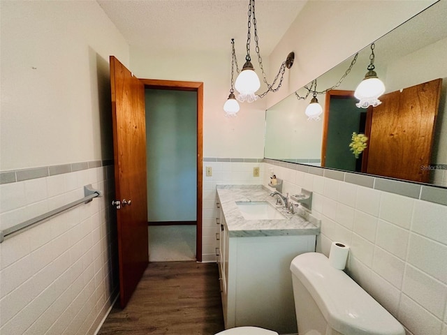 bathroom with a wainscoted wall, toilet, vanity, wood finished floors, and tile walls