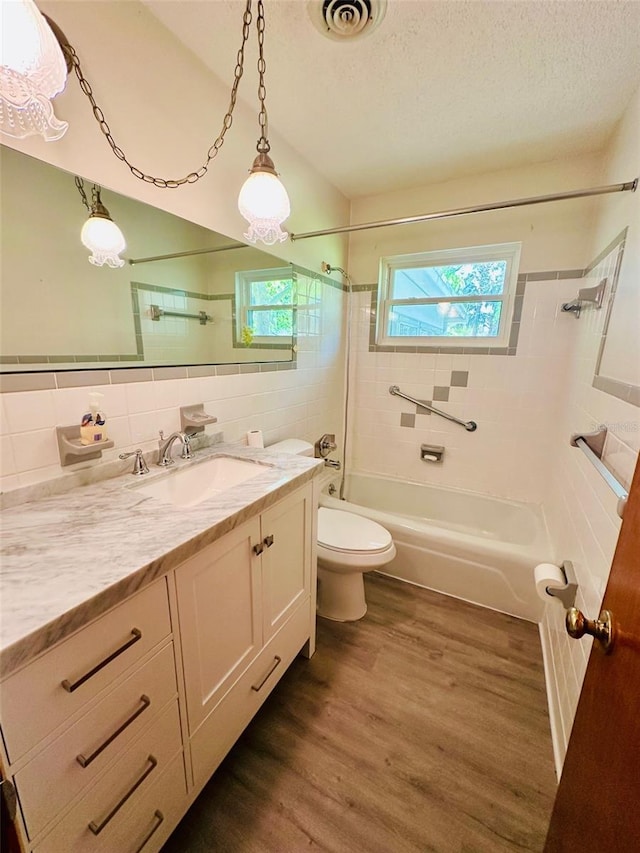 full bathroom with visible vents, a textured ceiling, shower / tub combination, wood finished floors, and tile walls